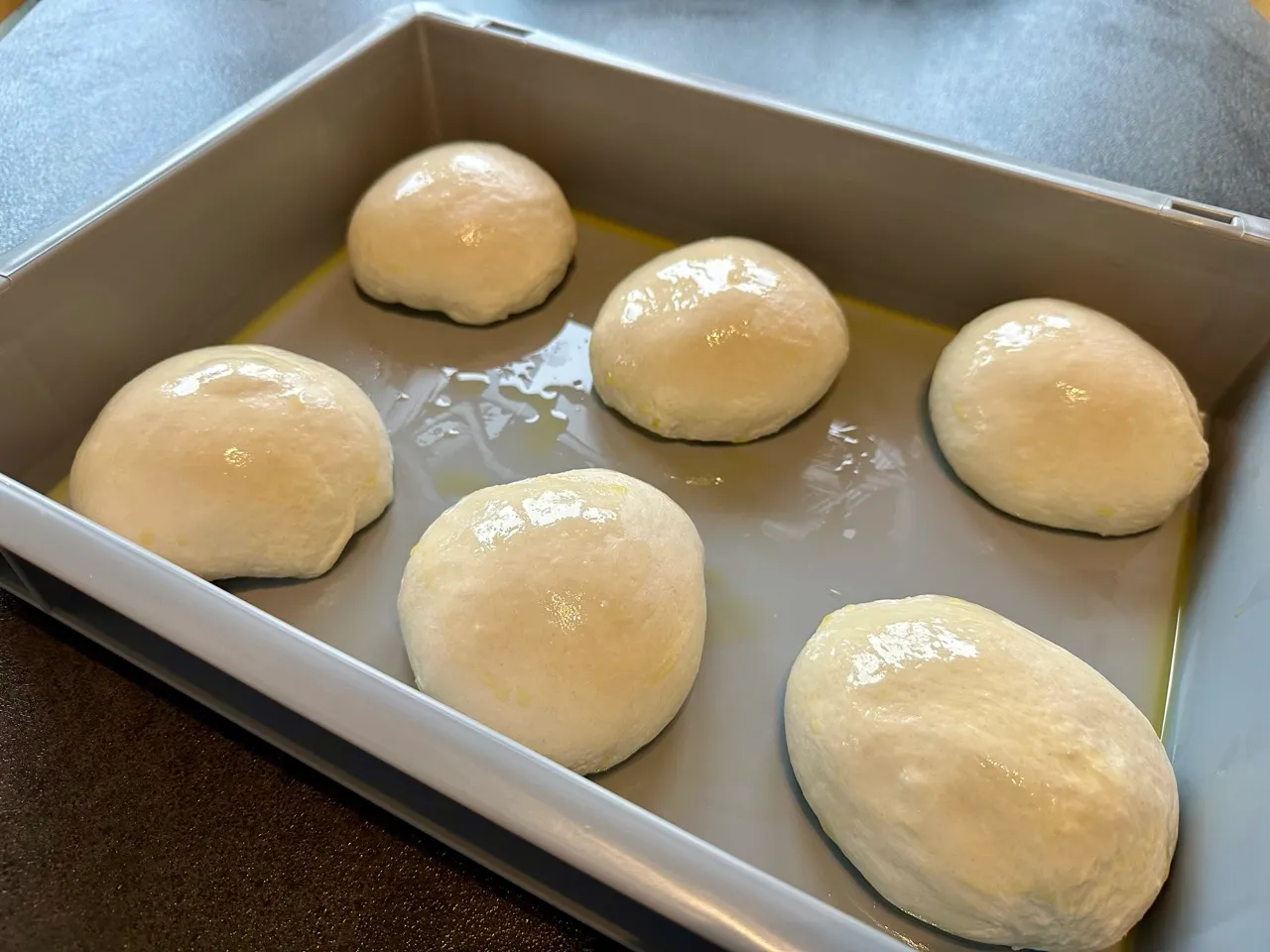 Quatre pâtons de pizza bien lisses et réguliers dans un bac de fermentation huilé après 24h de repos au réfrigérateur